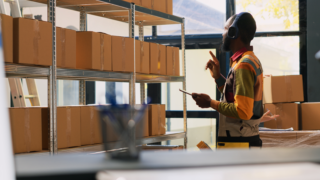 young-worker-organizing-products-depot-listening-music-headset-while-he-works-quality-control-warehouse-employee-checking-logistics-tablet-retail-store-delivery